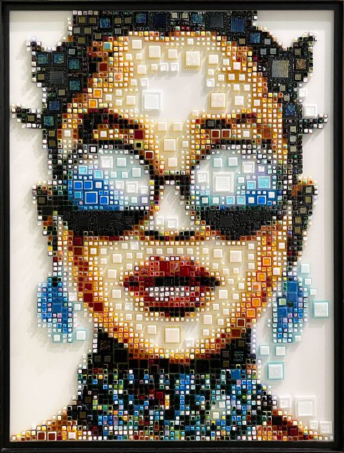 Woppi by Isabelle Scheltjens. Pieces of glass in different colors, sizes, and textures are melted together and applied like dots of paint used by pointillists to create Pop art portraits of modern celebrities, icons, and female faces. This portrait was inspired by American singer H.E.R.