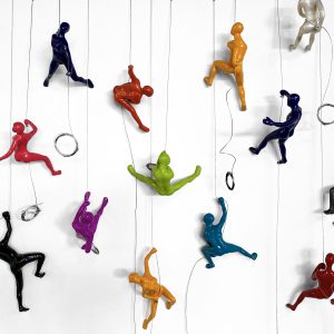 colorful wall climbers by Ancizar Marin. Different colored abstract figures climbing a white wall along a stainless steel cable