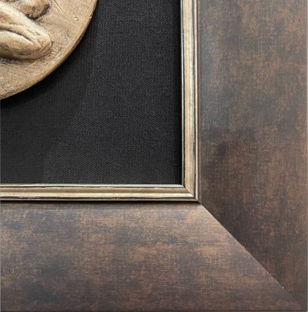 Bronze colored sculpture of a man and woman nude embracing. Framed with a black background and rustic bronze frame.